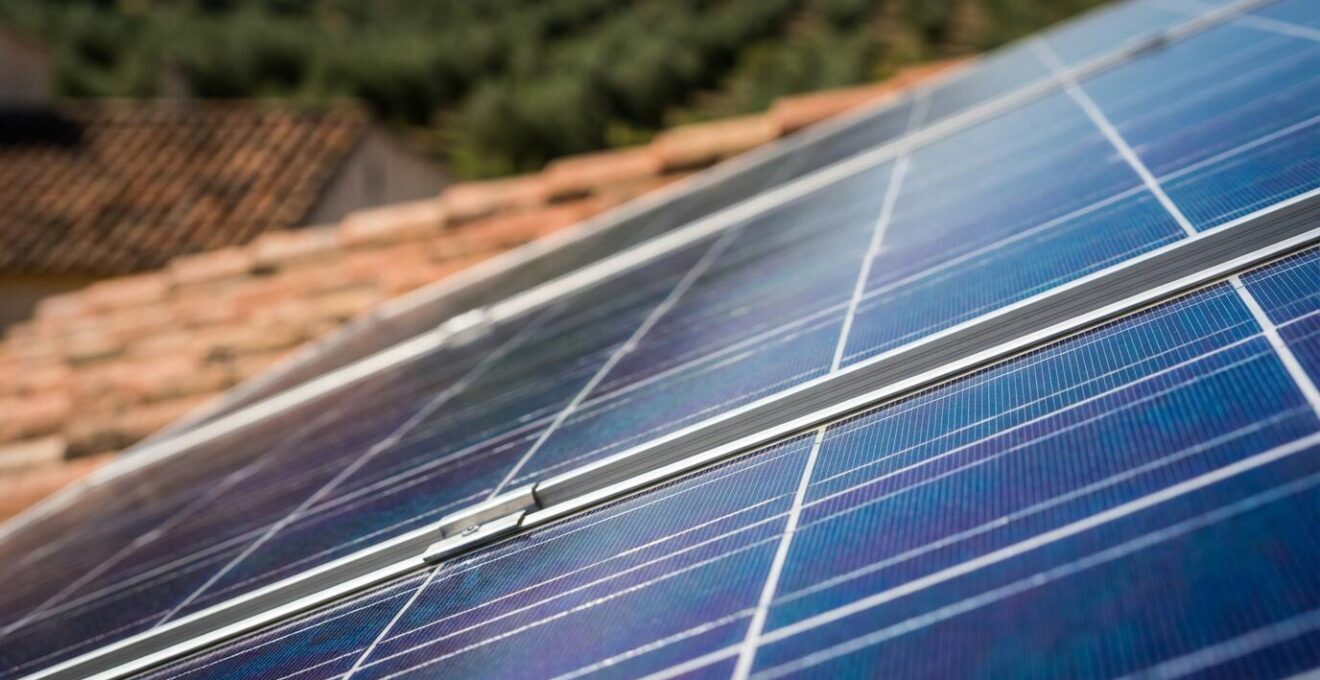 Sistema de paneles solares instalado en tejado de masía catalana con paisaje rural de fondo